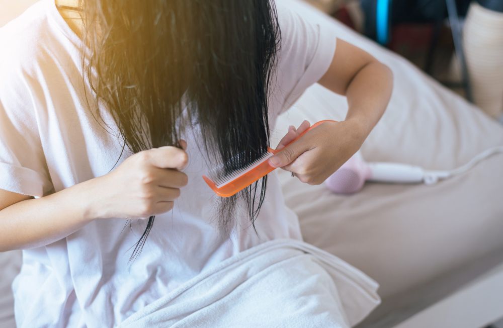 Žena pažljivo raščešljava dugu tamnu kosu narandžastim češljem kako bi smanjila zapetljavanje i lomljenje vlasi